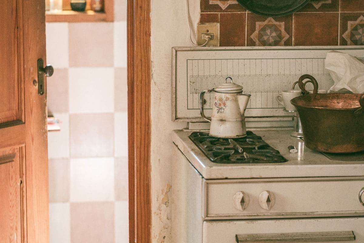 A dated kitchen with an old cooker and worn tiling, before renovation